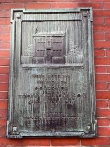 A metal plaque commemorating the site of Thomas Hutchinson's home. It has a line engraving of the outline of the house. 