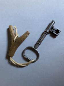 A metal key with a y-shaped piece of wood attached by a piece of twine