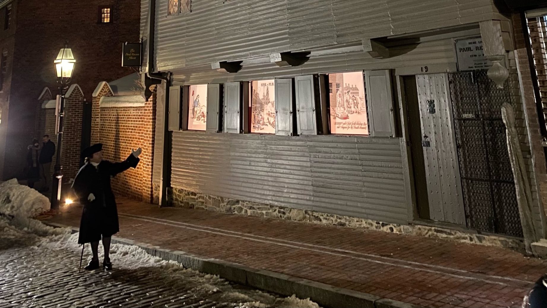 A picture showing the entire Revere House on a cloudy night. The building is dark grayish and clapboarded, under a cloudy night sky. The windows are illuminated.