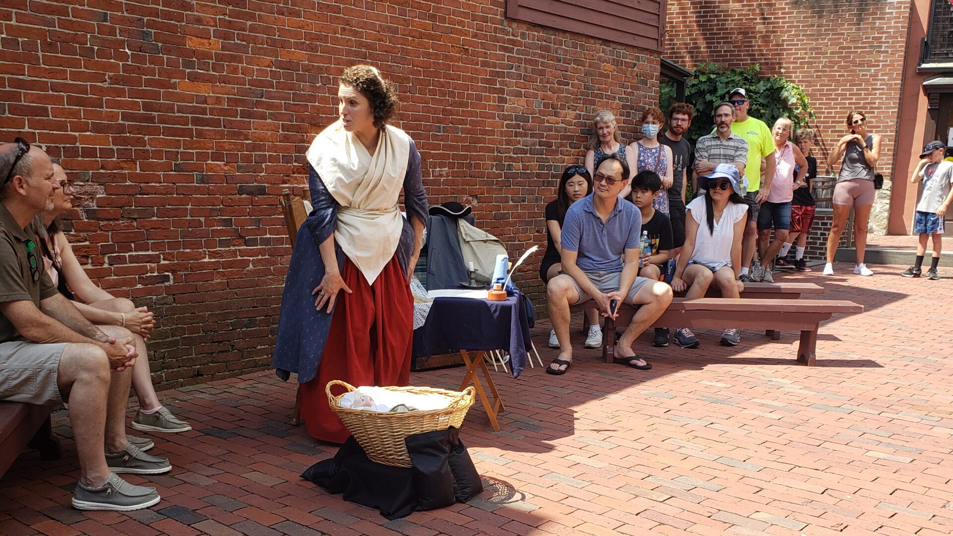 woman in colonial clothes speaking with people on benches