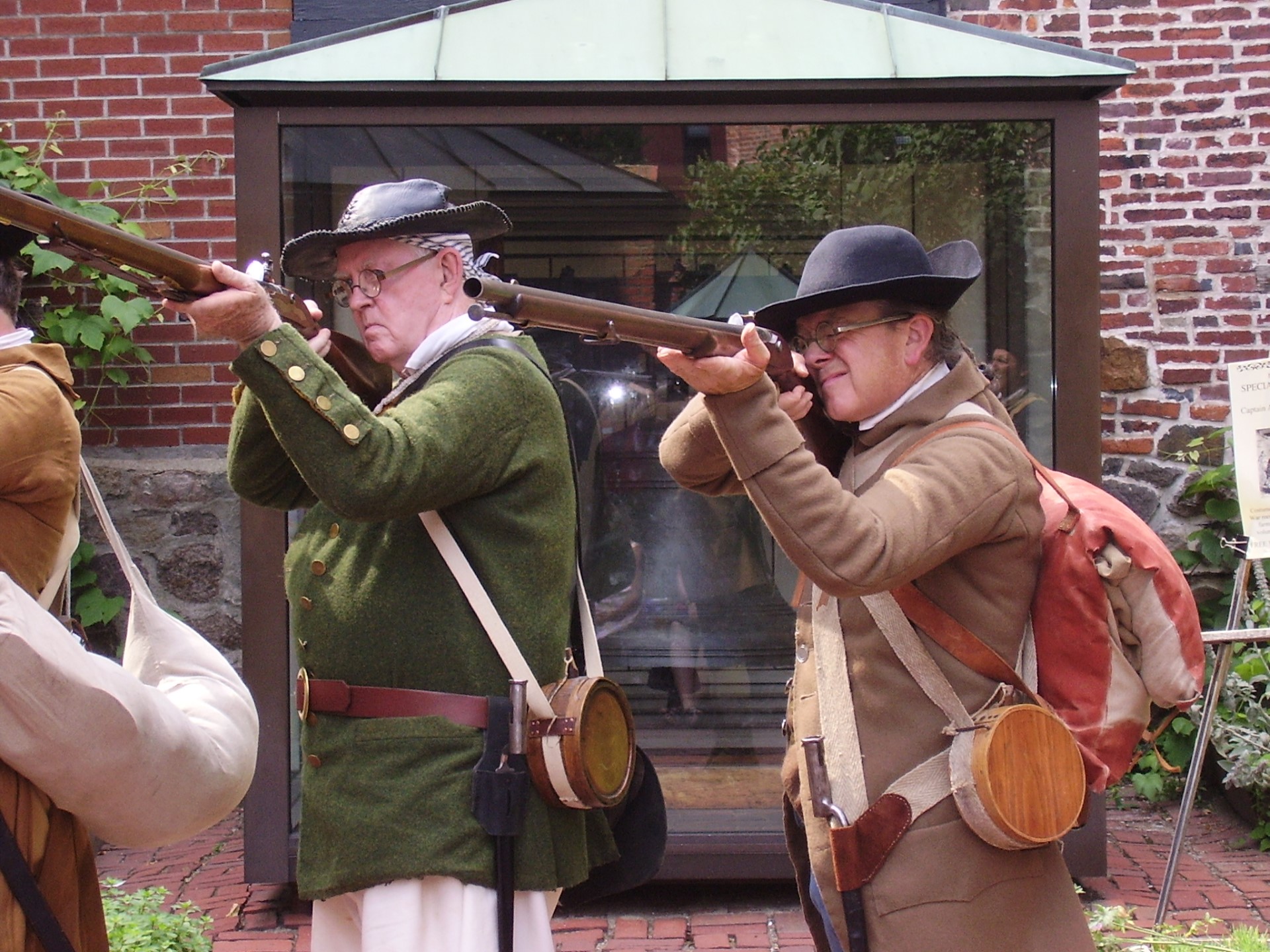two men in colonial militia clothing pointing muskets at the camera