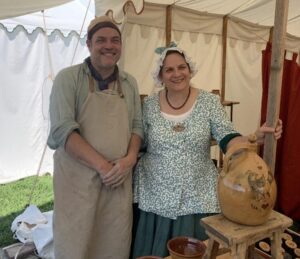 erich and janice standing behind a display of completed glazed pottery, dressed in colonial garb