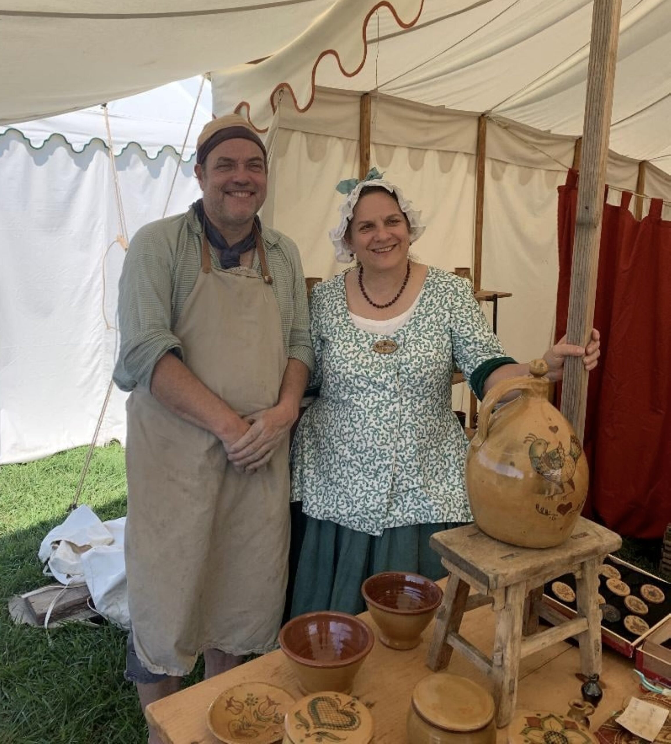 erich and janice standing behind a display of completed glazed pottery, dressed in colonial garb