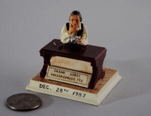 A figurine of Paul Revere at his workbench, next to a quarter for scale (the quarter is slightly larger than Revere).