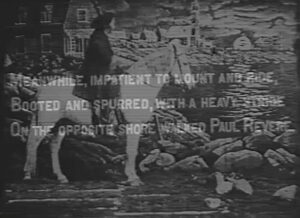 A still from The Midnight Ride of Paul Revere, showing Paul Revere on a horse watching the steeple of the Old North Church. The film is black and white, and grainy.