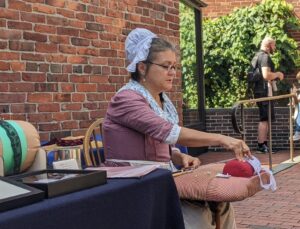 a woman in colonial garb demonstrating lacemaking