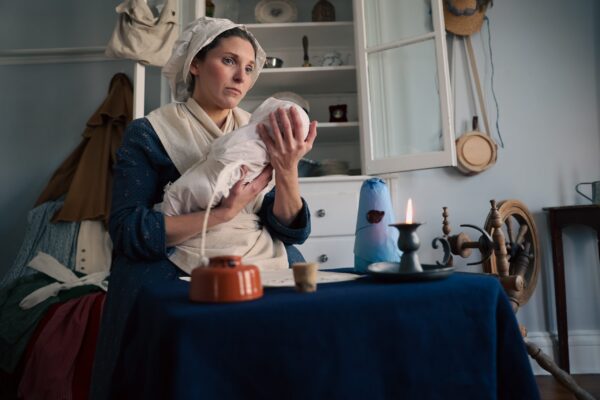 Photograph of Judith Kalaora as Rachel Revere holding a baby in her kitchen. Image credit: by History At Play™, LLC