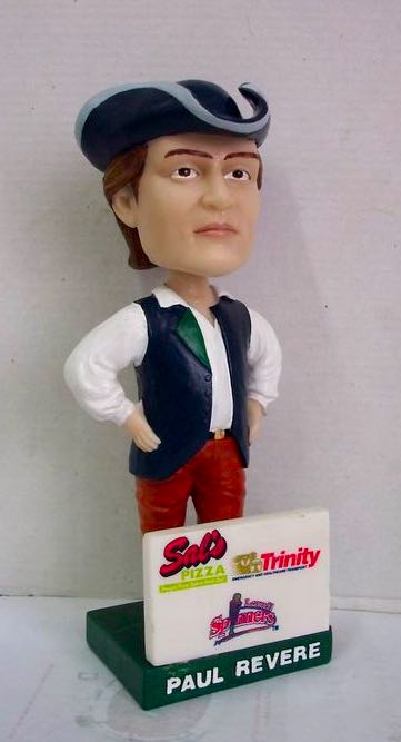 A bobblehead depicting Paul Revere. The base of the figure features the logos of the Lowell Spinners, Sal’s Pizza, and Trinity EMS.