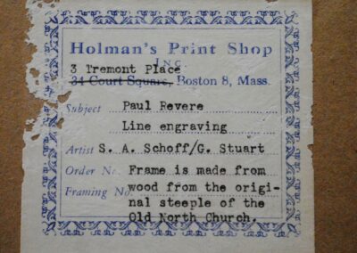 The back of a framed engraving with a label which reads “Holman’s Print Shop” with the address below and then a description of the artwork being sold.
