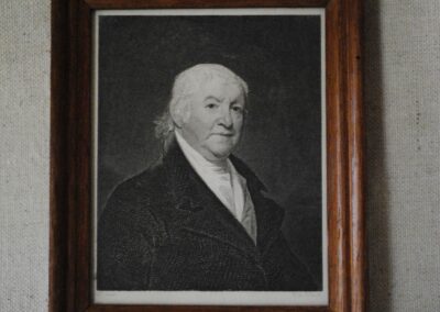 A black-and-white picture of an older Paul Revere, framed with wood and attached with a small metal ring at the top.
