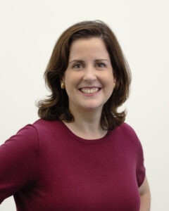 Nonie Gadsden, a white woman in a burgundy blouse. She is on a plain background and she's smiling.