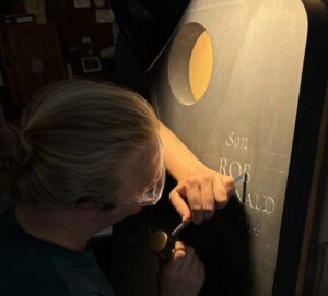 Michael Brache carving a gravestone with a chisel in dramatic low lighting